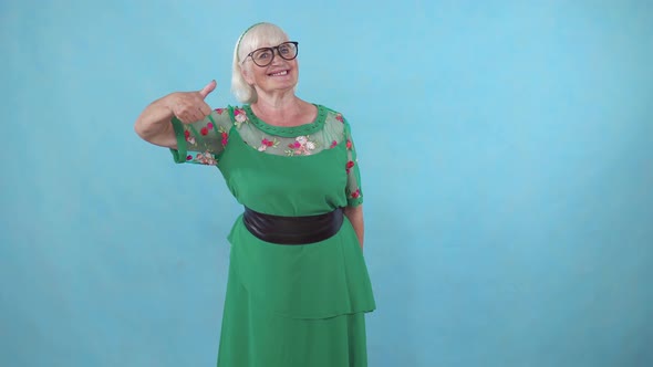 Older Woman in Glasses Shows with Approval Finger Up on Blue Background