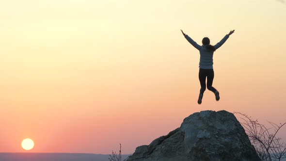 Silhouette of a woman hiker jumping alone on big stone at sunset in mountains. Female 