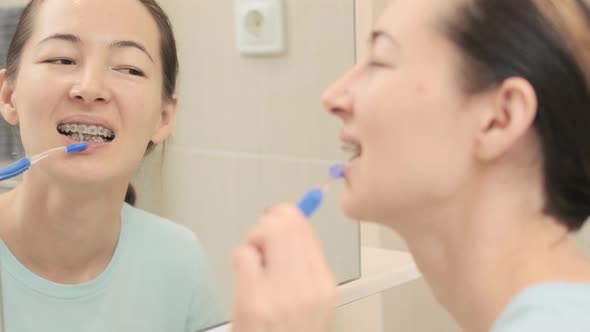 Young Woman with Braces Cleans Her Teeth with a Special Dental Brush Before Mirror