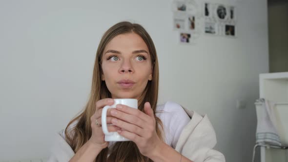 Young blond woman drinks tea in the white kitchen in good mood