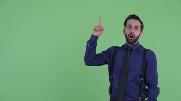 Happy Young Bearded Persian Businessman Pointing Up and Looking Surprised