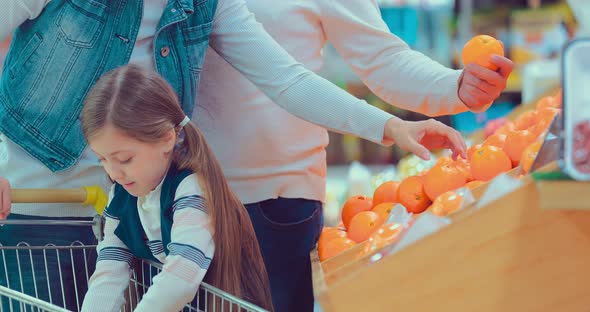 Closeup of Little Daughter Choosing Fruits in Supermarket