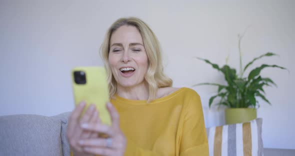 Mature woman sitting on sofa making video call on smartphone