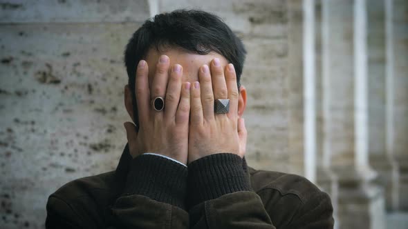 Desperate young man covering his face with hands in the street. Problems,worries