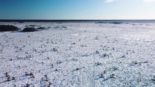 Aerial birdseye view of snowy bog landscape with hiking trail and frozen lakes in sunny winter day,