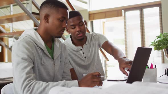 Two african american teenage twin brothers using a laptop and talking