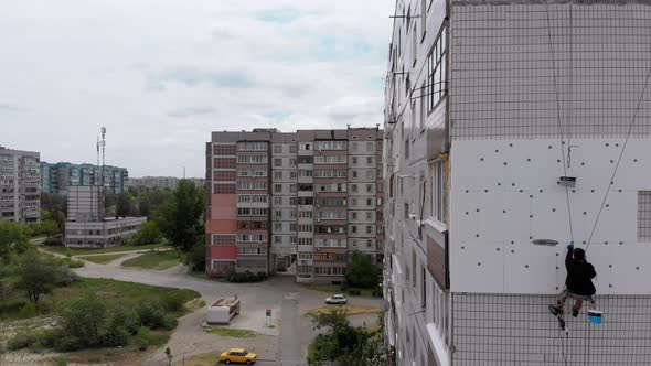 Aerial View on Industrial Climber Suspended on Ropes Performs Work on Insulation of Facade of High