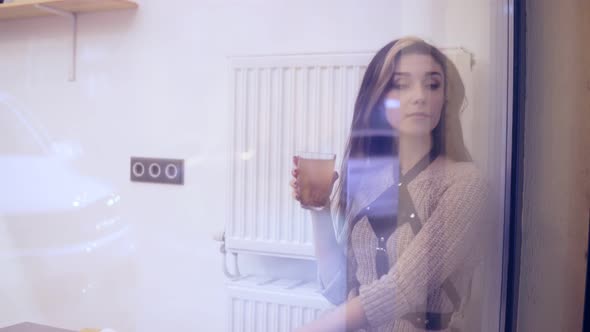 Woman Viewed Through Window Drinks Hot Tea and Takes Her Smartphone