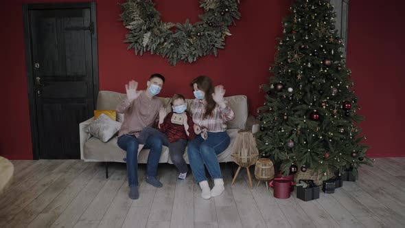 Family Sittingon Sofa Near Christmas Tree in Pandemic and Waving at Camera