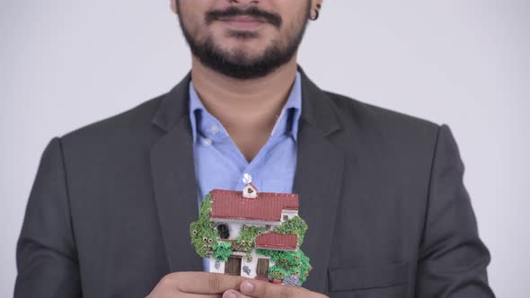 Young Happy Bearded Indian Businessman Holding House Figurine