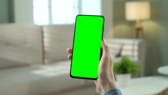 Close Up View of Woman at Modern Room Sitting on a Chair Using Phone With Green Mock-up Screen