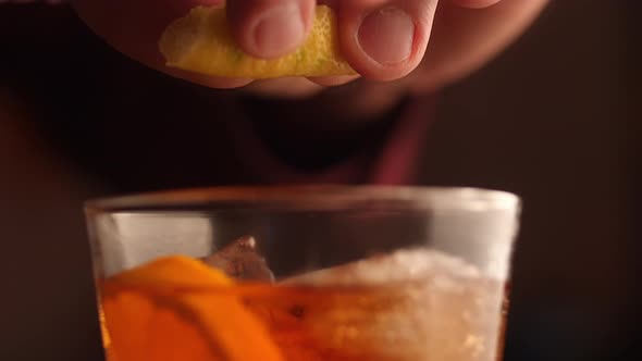Barman squeezes the lemon peel into the cocktail. Macro shot in slow motion.