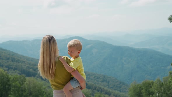 Woman Holds Little Son and Adjusts Hair at Mountain Resort