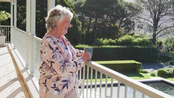 Caucasian senior woman holding coffee cup smiling while standing in the balcony at home