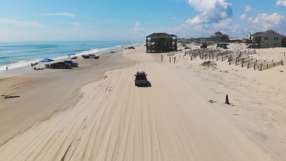 Drone following black suv on Outer Banks Corolla 4x4 beach, houses can be seen inland.