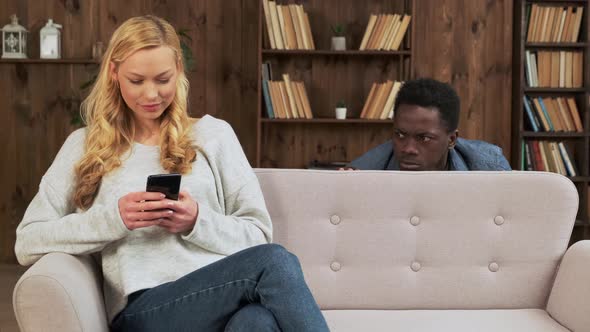 Cheater Woman Dating Online with a Smart Phone and Boyfriend is Spying Sitting on a Sofa at Home
