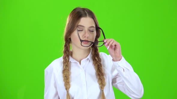 Schoolgirl in a Plaid Skirt Takes Off Her Glasses and Yawns. Green Screen