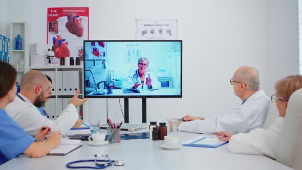 Team of Doctors Having Video Conference Sitting at Desk in Hospital Meeting Room