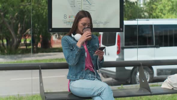 Young Stylish Woman Waiting for the Public Transport and Drink Coffee