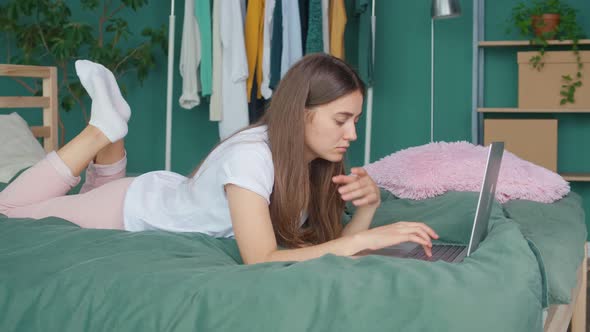 Woman Student Freelancer Studies Works Online on a Laptop at Home in Bed