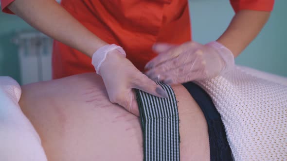 Woman Puts Belt Onto Woman Belly with Striae Distensae