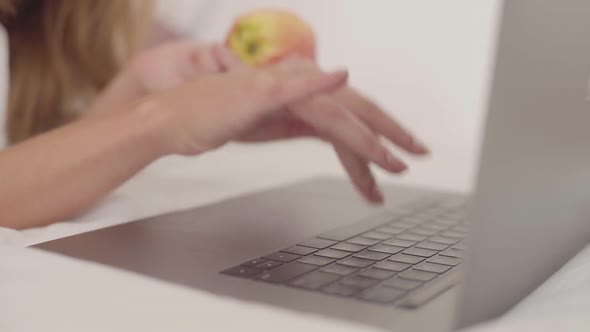 Close-up of a Young Caucasian Female Hand Typing on Laptop. Woman Holding the Red Apple