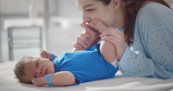 Loving Mother Caring for Her Newborn Baby Kissing His Feet