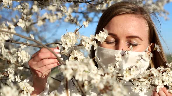 A girl in a medical mask stands near a flowering tree. Coronavirus epidemic. COVID-19