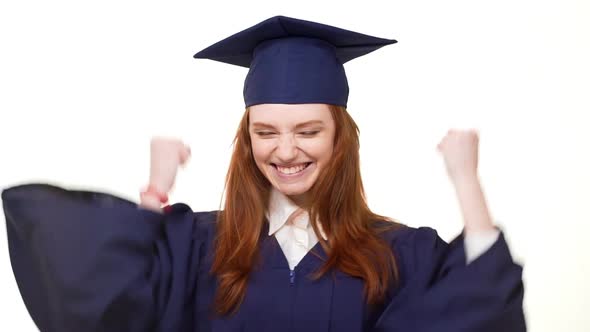 Young Attractive Caucasian Redhead Graduate Girl in Blue Academical Square Cap and Robe Rejoicing