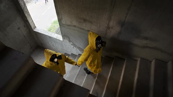 Woman in Gas Mask Gives Hand to Man to Follow Me Him in Abandoned Building on Stairs