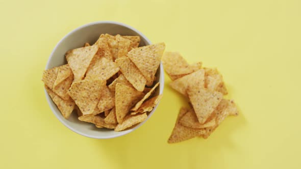 Close up of nachos falling in a bowl on yellow surface