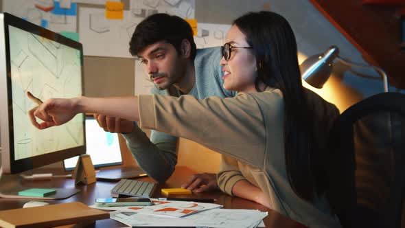 Male Project manager talking with asian female worker looking at computer screen discussing project