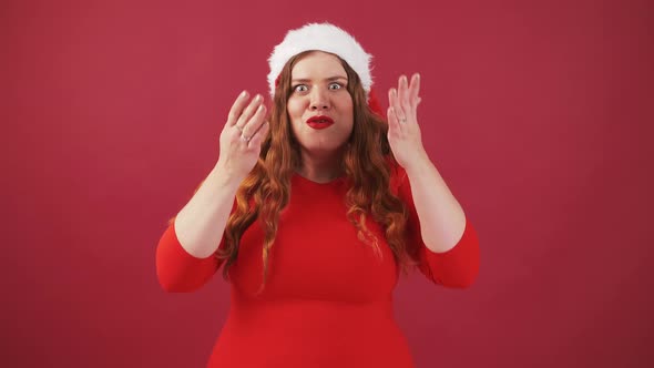 Emotional Young Plus Size Woman in Christmas Hat with Shocked Expression Keeping Palms on Cheek Red