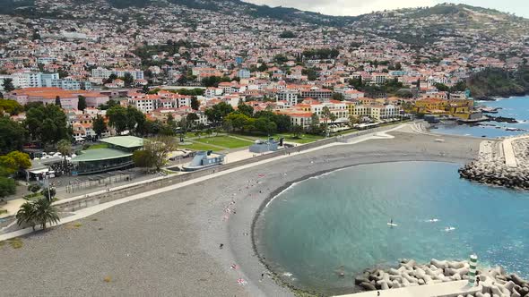 Aerial pan shot of Funchal coastal town in Madeira island, Portugal surrounded by a mountain range a