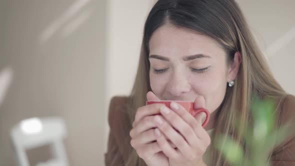 Closeup of Young Caucasian Woman Smelling Delicious Tea or Cofee and Smiling