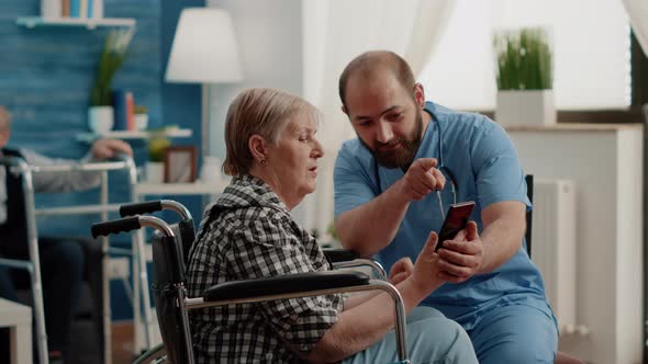 Man Nurse Teaching Retired Woman with Handicap to Use Smartphone