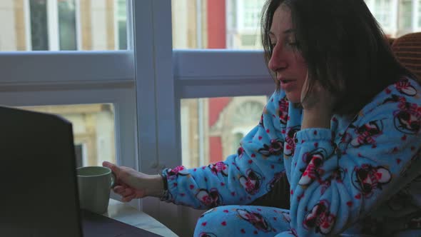 a Girl in Blue Pajamas Sits By the Window Behind a Nautbook and Cries