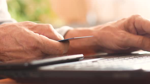 Close-up of a bank card and laptop keyboard in the hands of an elderly man