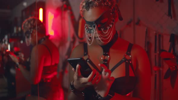 African Woman in Bdsm Lingerie and Mask Surfing Internet on Smartphone