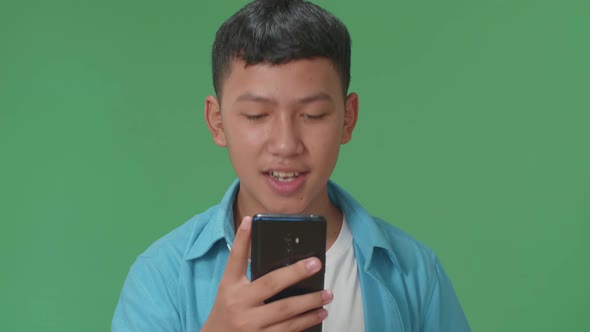 Smiling Young Asian Boy Using Mobile Phone In Green Screen Studio alt