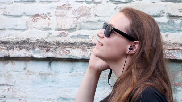 Young attractive girl in black t-shirt sunglasses in rock style on urban background listening music