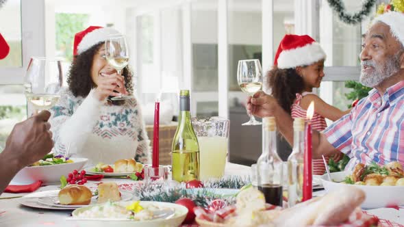 Happy african american multi generation family wearing santa hats and celebrating holiday meal