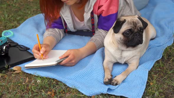 Girl Laying on a Lawn and Writing, Her Pug Laying Beside