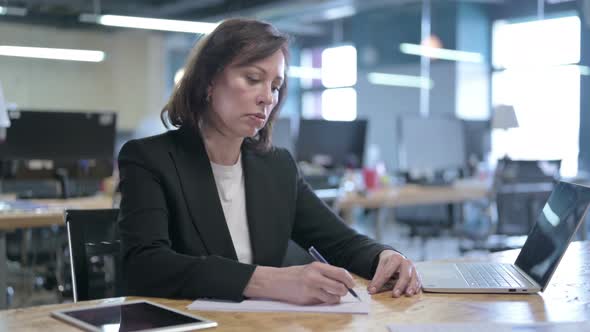 Serious Middle Aged Businesswoman Writing on Papers While Working in Office