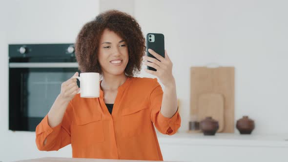 African American Girl Blogger Woman Influencer Holding Cup of Tea Coffee Shows to Camera Makes Photo