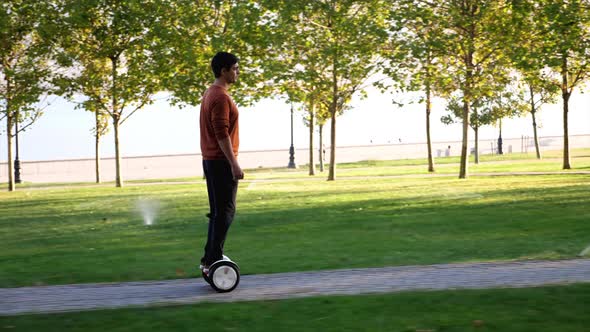 A Man is Riding Segway at the City on Seafront Side View