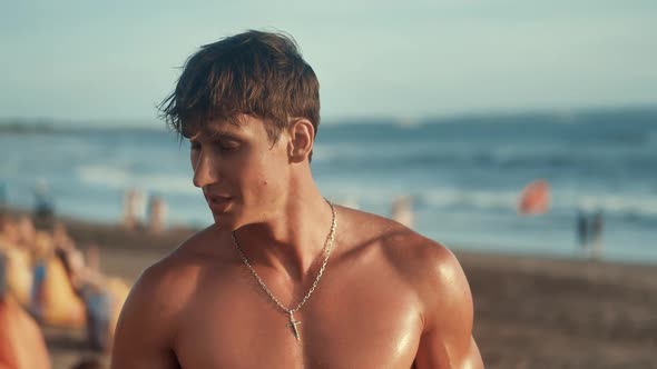 Portrait of Handsome Muscular Man Puts on Sunglasses on the Beach at Sunset