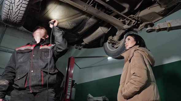 Worker and Client with Flashlight Check Automobile Bottom
