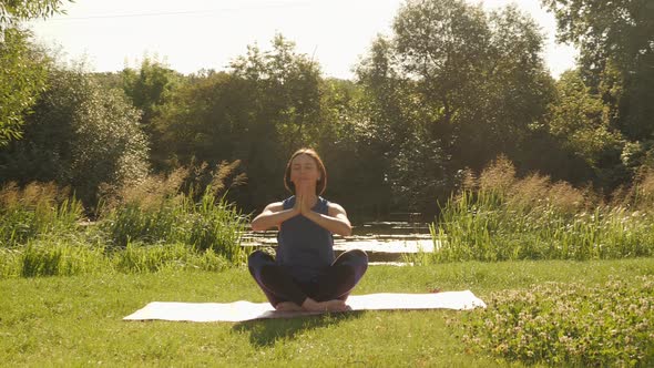 Woman sitting in lotus position on yoga mat and feeling harmony of her body and nature