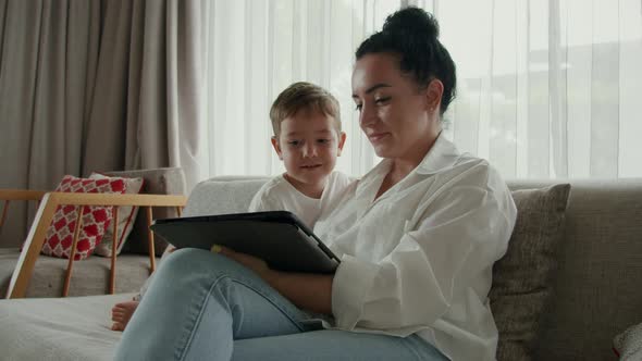 Happy Mom and Cute Son Little Child Mother Plays with Her Baby at Home Relaxing Using Smartphone